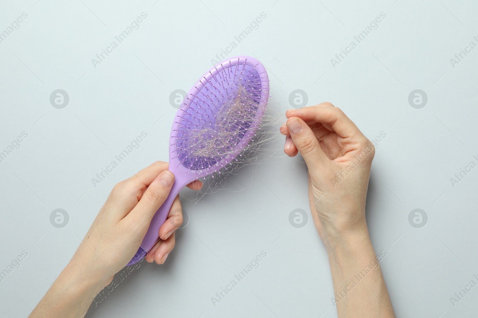 Photo of Woman taking her lost hair from brush on grey background, top view. Alopecia problem