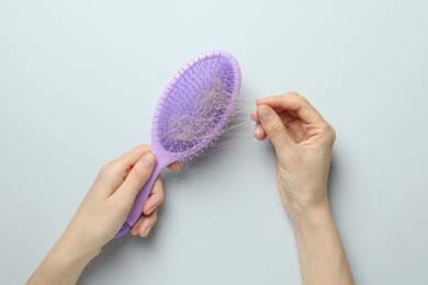 Woman taking her lost hair from brush on grey background, top view. Alopecia problem