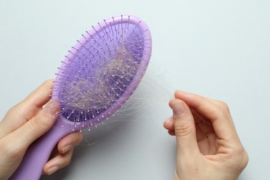 Photo of Woman taking her lost hair from brush on grey background, top view. Alopecia problem