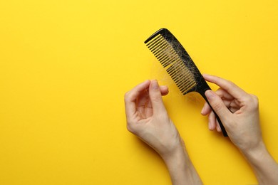 Woman taking her lost hair from comb on yellow background, top view. Space for text