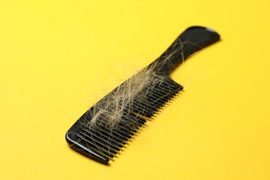 Photo of One comb with lost hair on yellow background, closeup. Alopecia problem