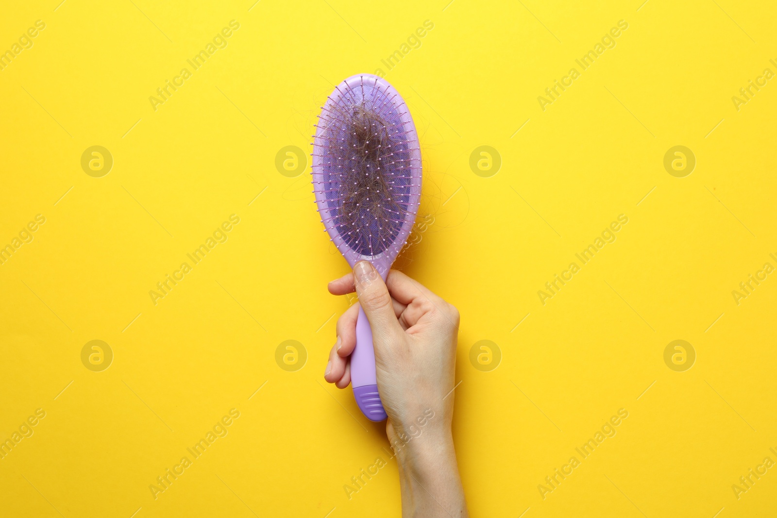 Photo of Woman with brush and lost hair on yellow background, top view. Alopecia problem