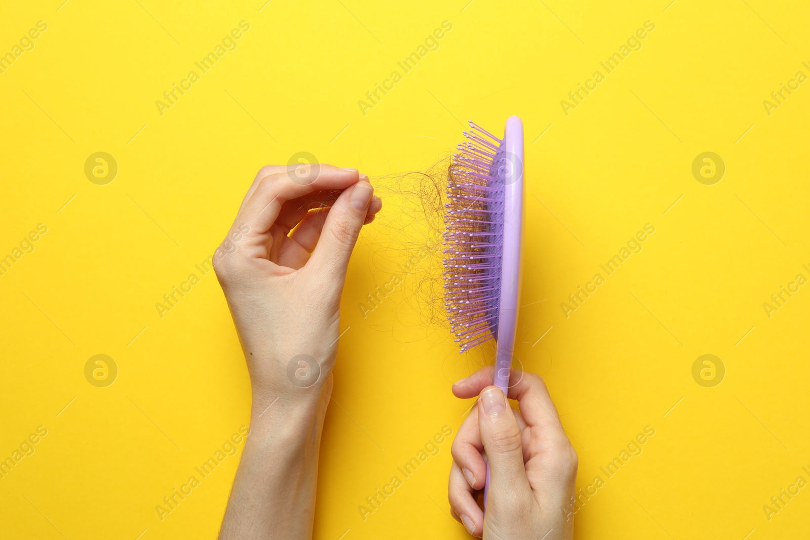 Photo of Woman taking her lost hair from brush on yellow background, top view. Alopecia problem