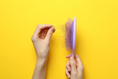 Woman taking her lost hair from brush on yellow background, top view. Alopecia problem