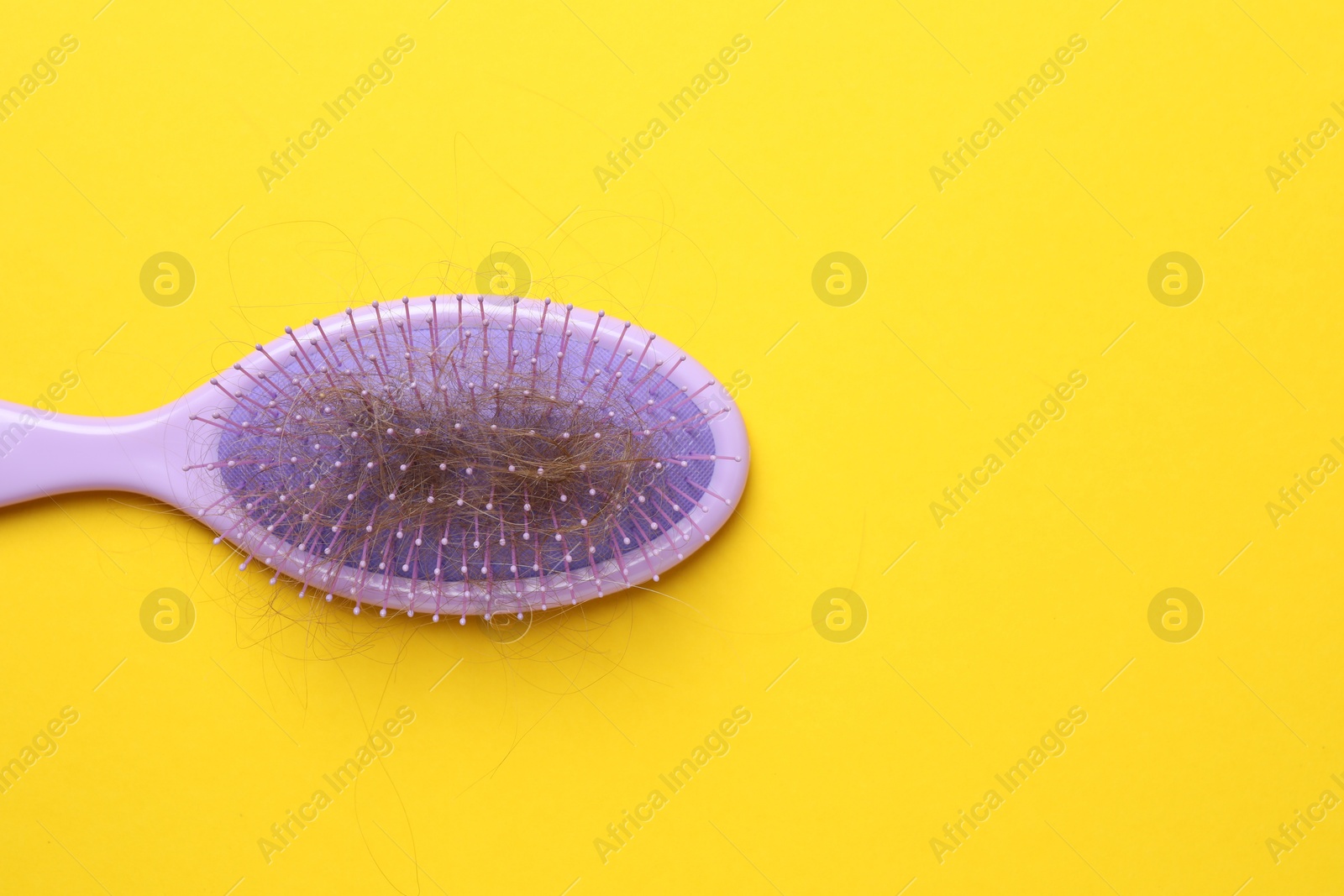 Photo of One brush with lost hair on yellow background, top view. Space for text