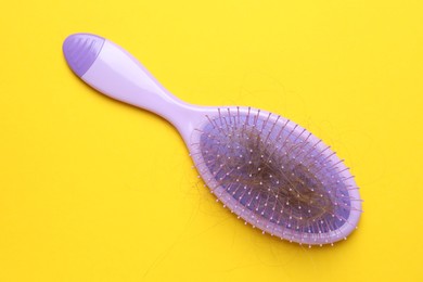 Photo of One brush with lost hair on yellow background, top view. Alopecia problem