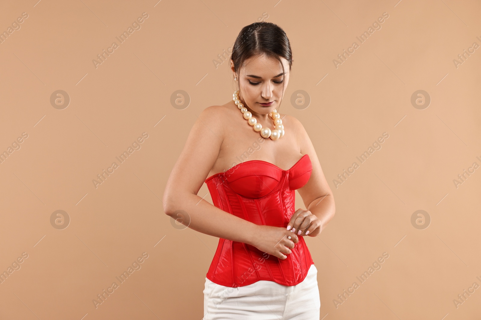 Photo of Beautiful woman in red corset posing on beige background