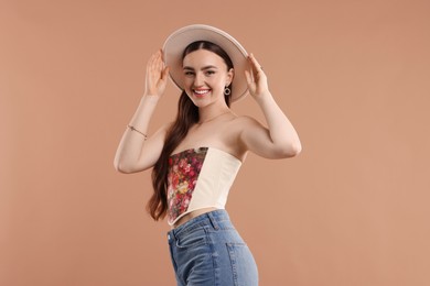 Photo of Smiling woman in stylish corset and hat posing on beige background