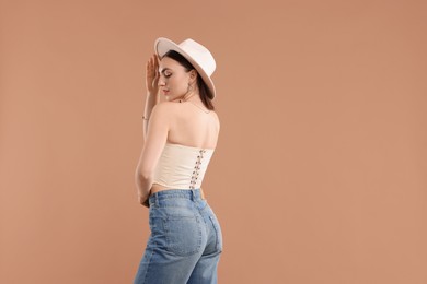 Photo of Beautiful woman in stylish corset and hat posing on beige background. Space for text