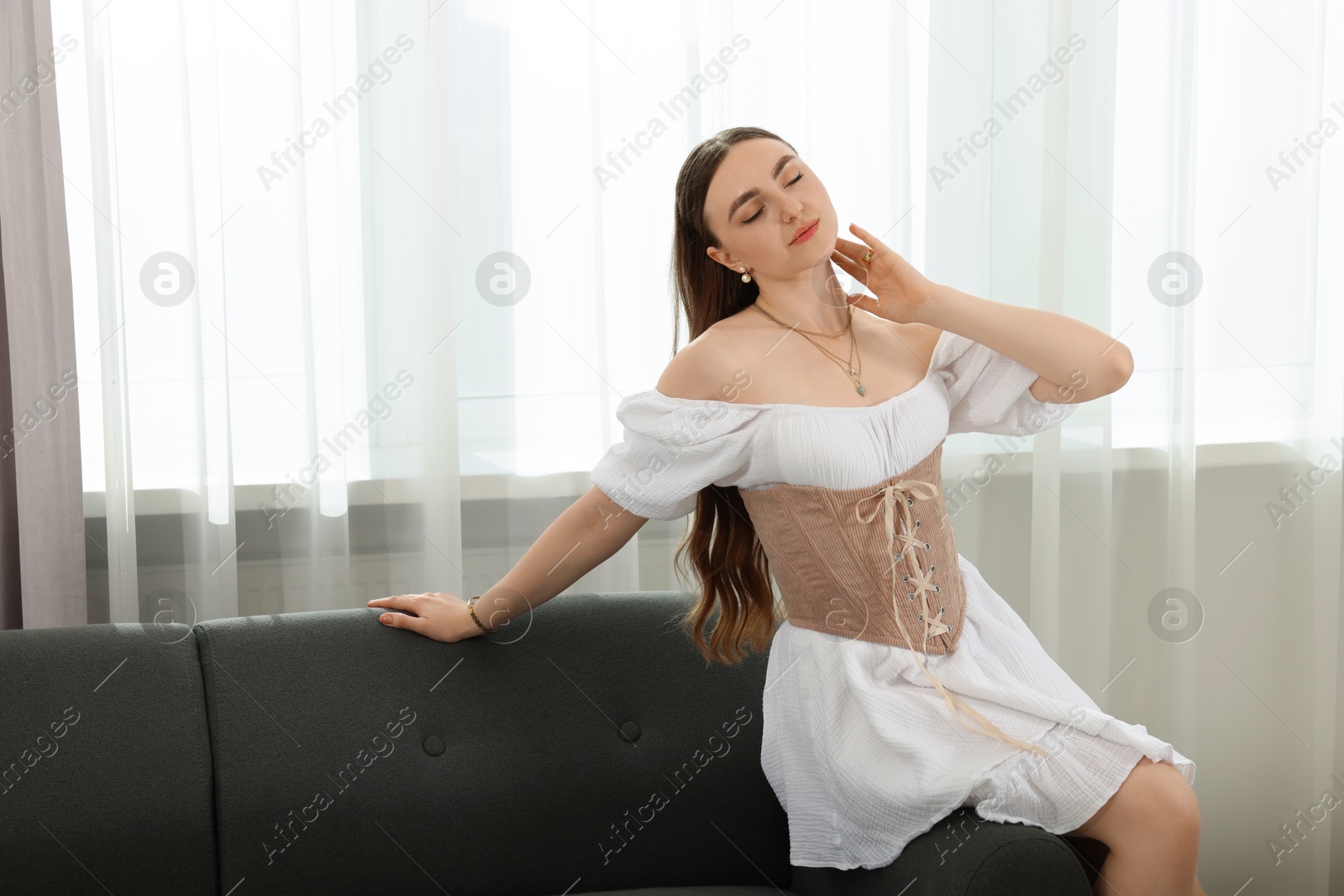 Photo of Beautiful woman in stylish corset posing on sofa indoors. Space for text