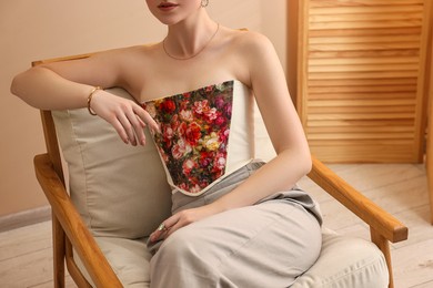 Photo of Woman in stylish corset on armchair indoors, closeup