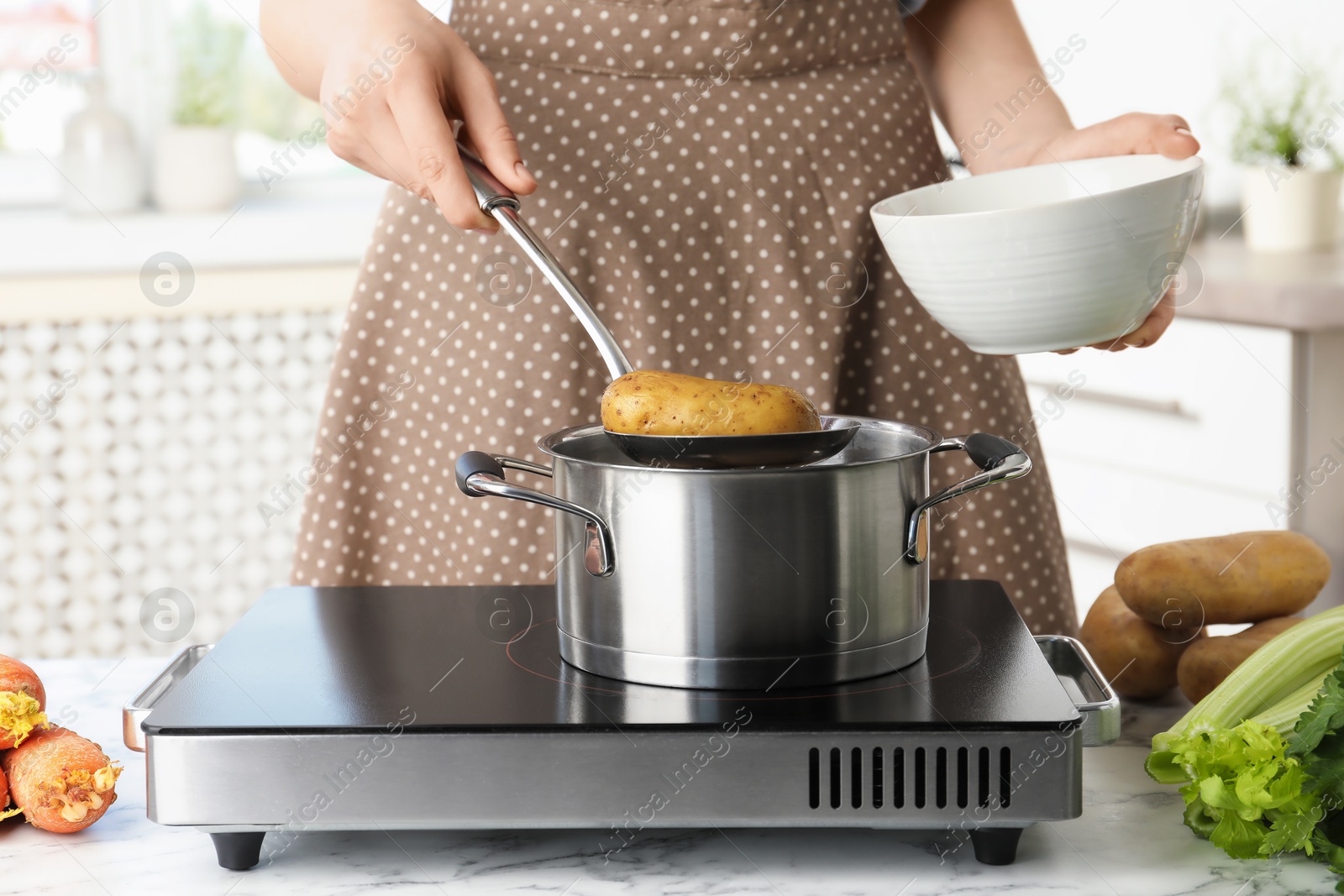 Photo of Woman putting potato into metal pot on stove, closeup