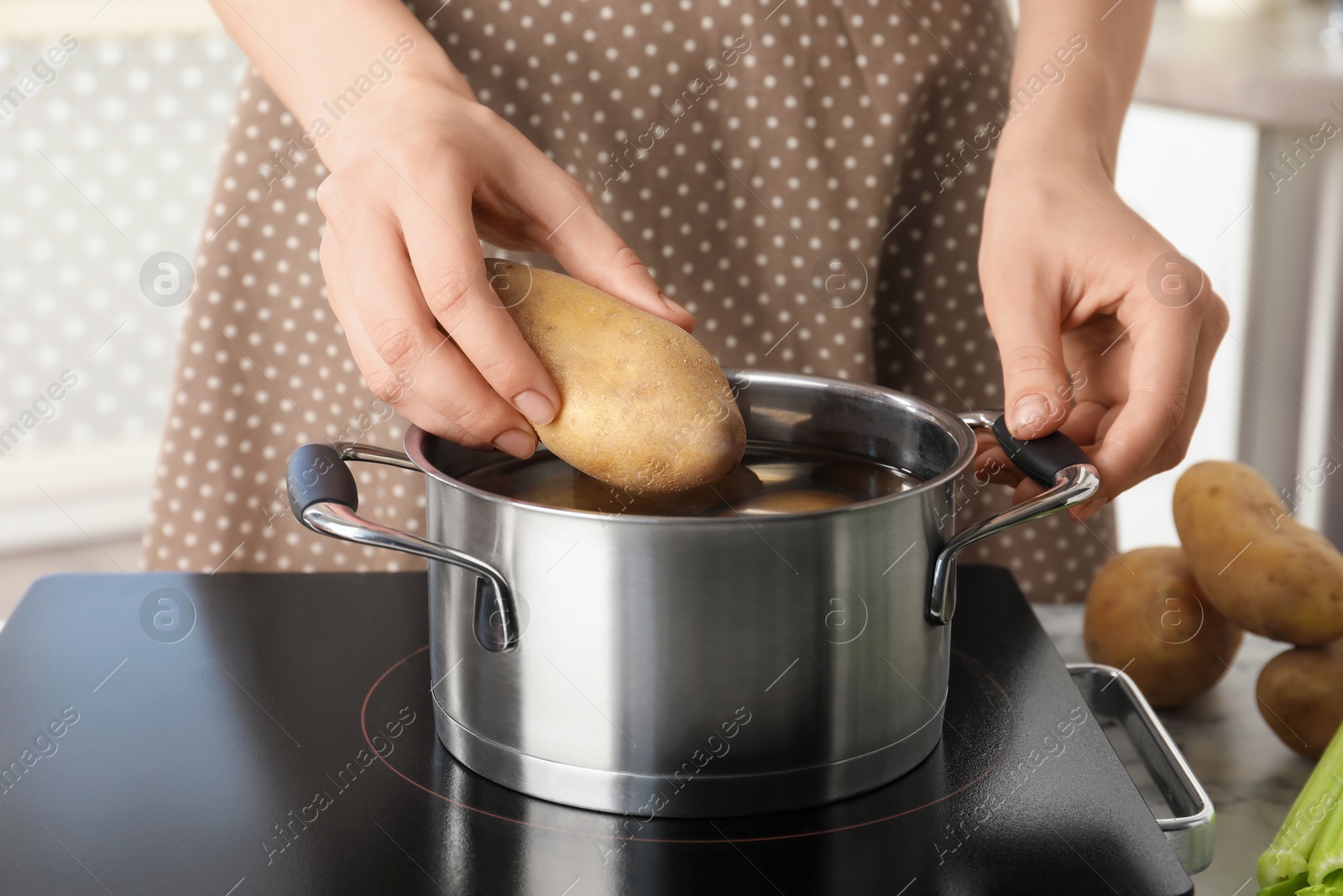 Photo of Woman putting potato into metal pot on stove, closeup