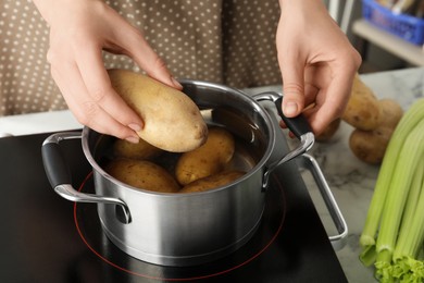 Photo of Woman putting potato into metal pot on stove, closeup