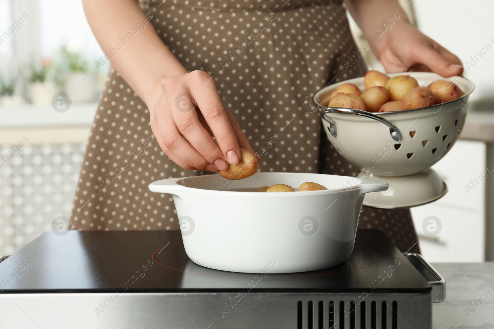 Photo of Woman putting potato into metal pot on stove, closeup