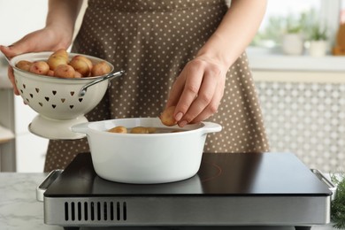 Woman putting potato into metal pot on stove, closeup