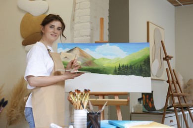 Photo of Portrait of smiling woman drawing landscape with brush in studio