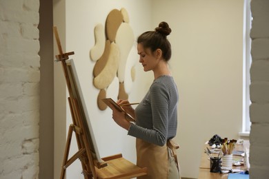 Photo of Woman with brush and palette near easel in drawing studio