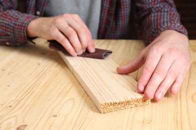 Photo of Man polishing wooden plank with sandpaper at table, closeup