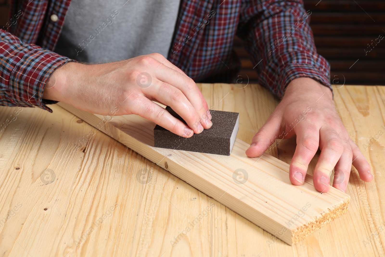 Photo of Man polishing wooden plank with sandpaper at table, closeup