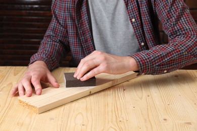 Photo of Man polishing wooden plank with sandpaper at table, closeup