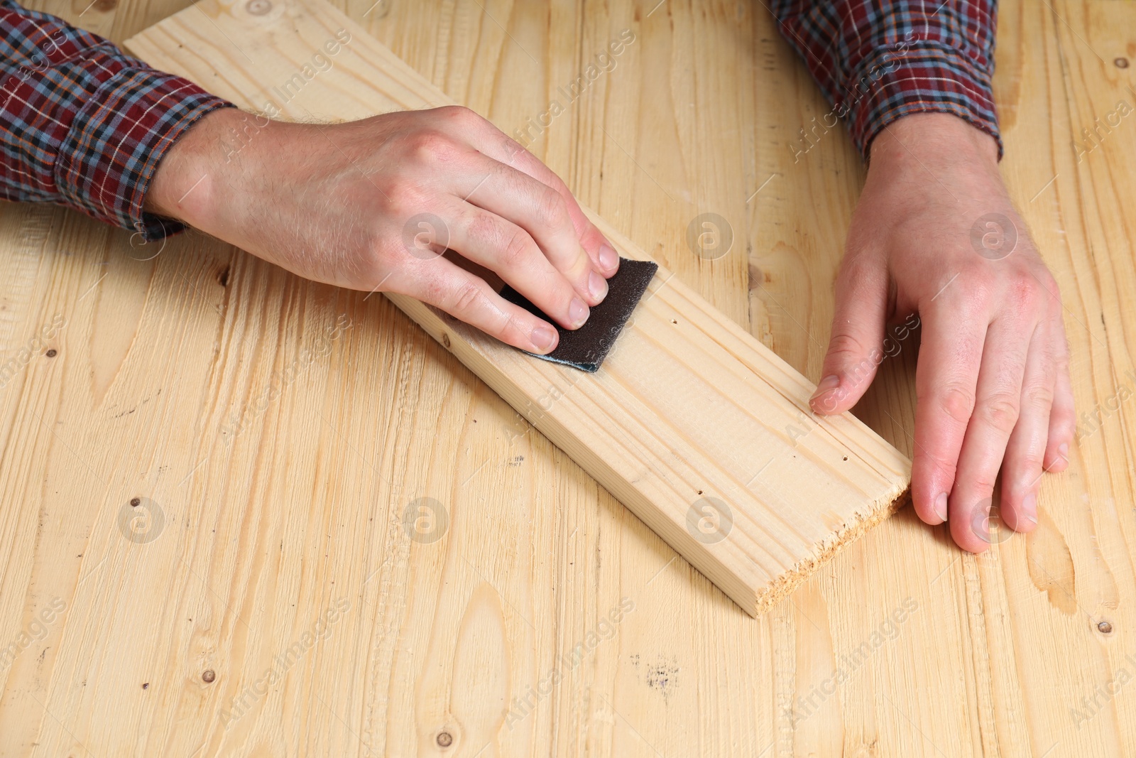 Photo of Man polishing wooden plank with sandpaper at table, closeup