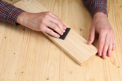 Man polishing wooden plank with sandpaper at table, closeup