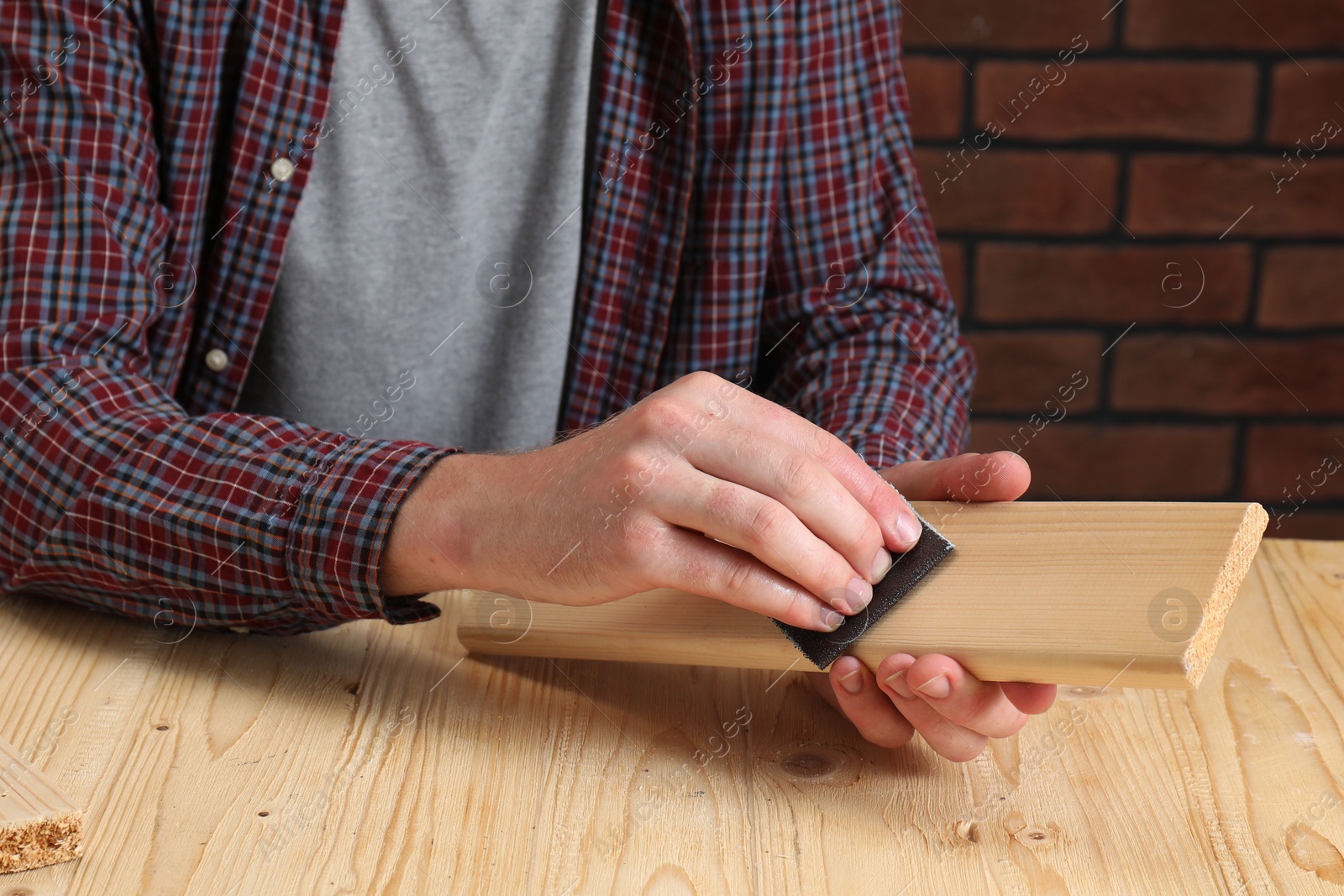 Photo of Man polishing wooden plank with sandpaper at table, closeup