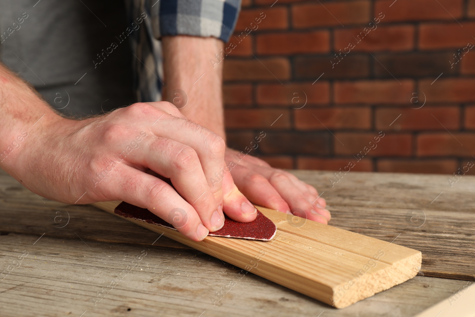 Photo of Man polishing wooden plank with sandpaper at table, closeup