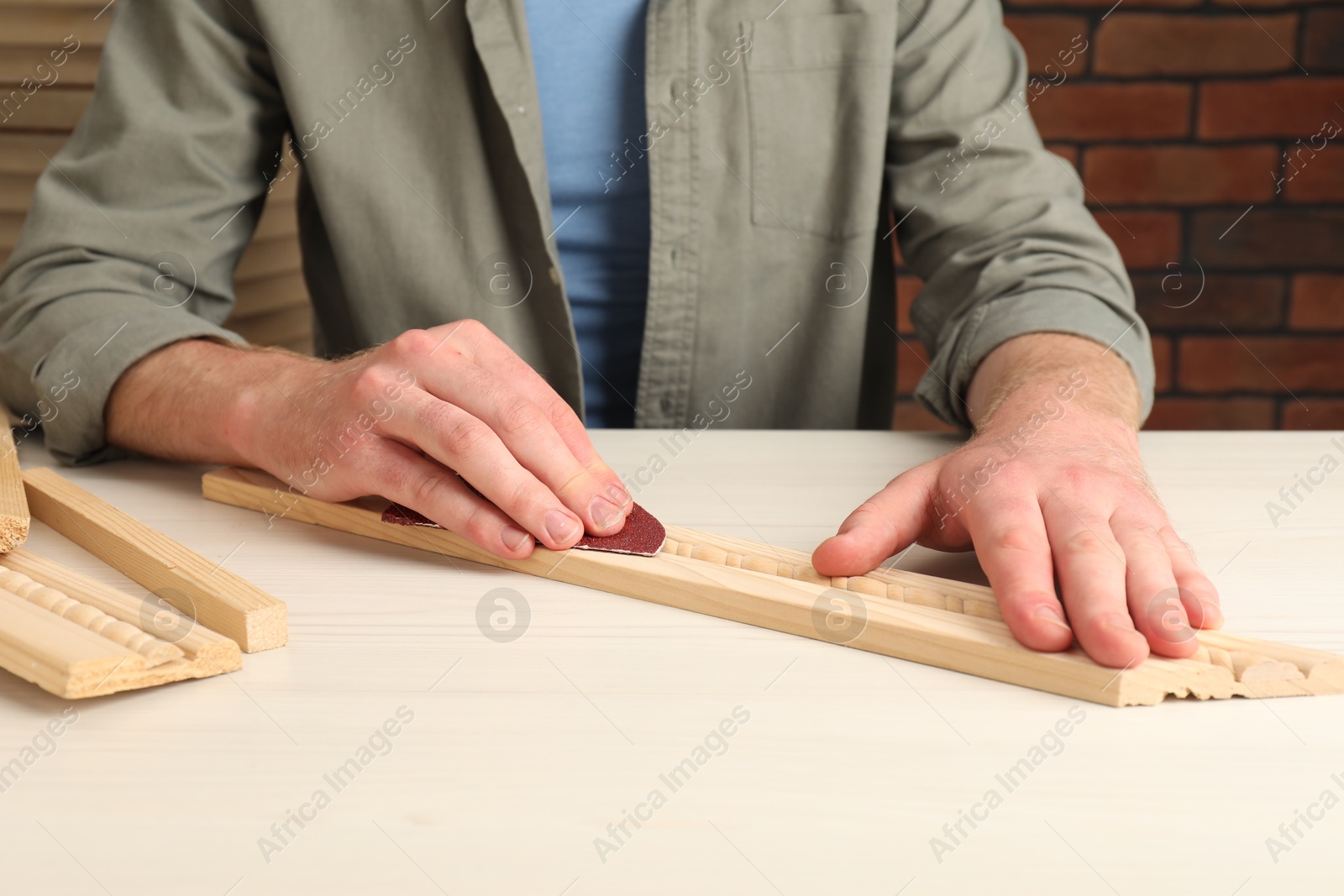 Photo of Man polishing wooden plank with sandpaper at table, closeup