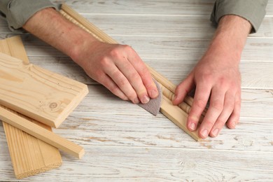 Photo of Man polishing wooden plank with sandpaper at table, closeup