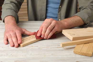 Photo of Man polishing wooden plank with sandpaper at table, closeup