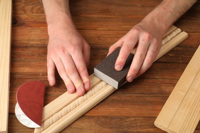 Photo of Man polishing wooden plank with sandpaper at table, closeup