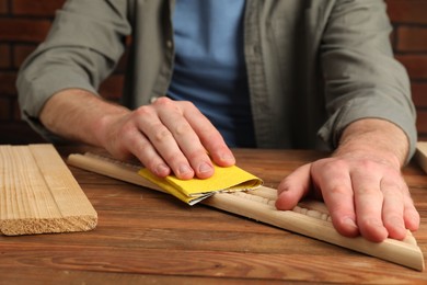 Photo of Man polishing wooden plank with sandpaper at table, closeup