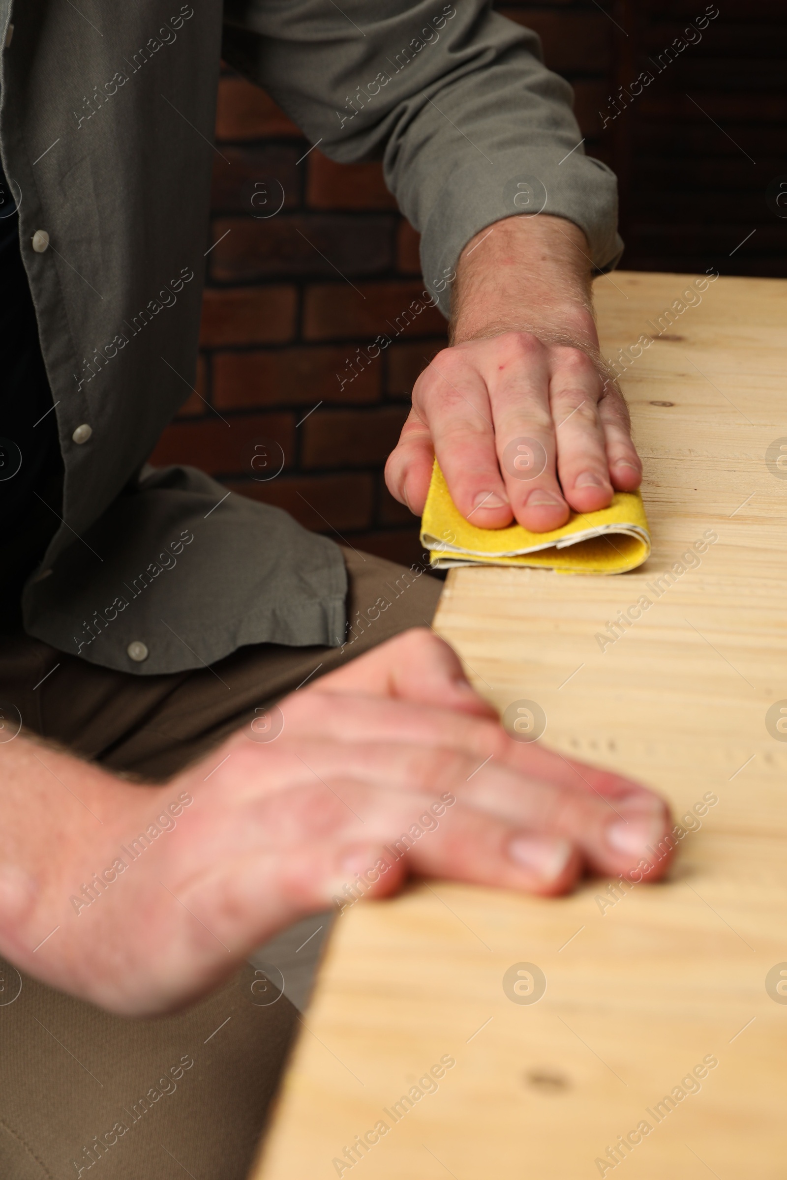 Photo of Man polishing wooden plank with sandpaper at table, closeup