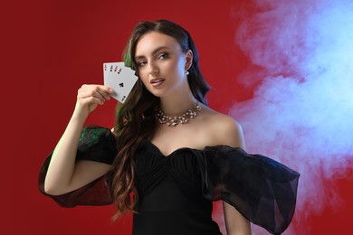 Photo of Poker game. Charming woman with playing cards on red background in color lights and smoke