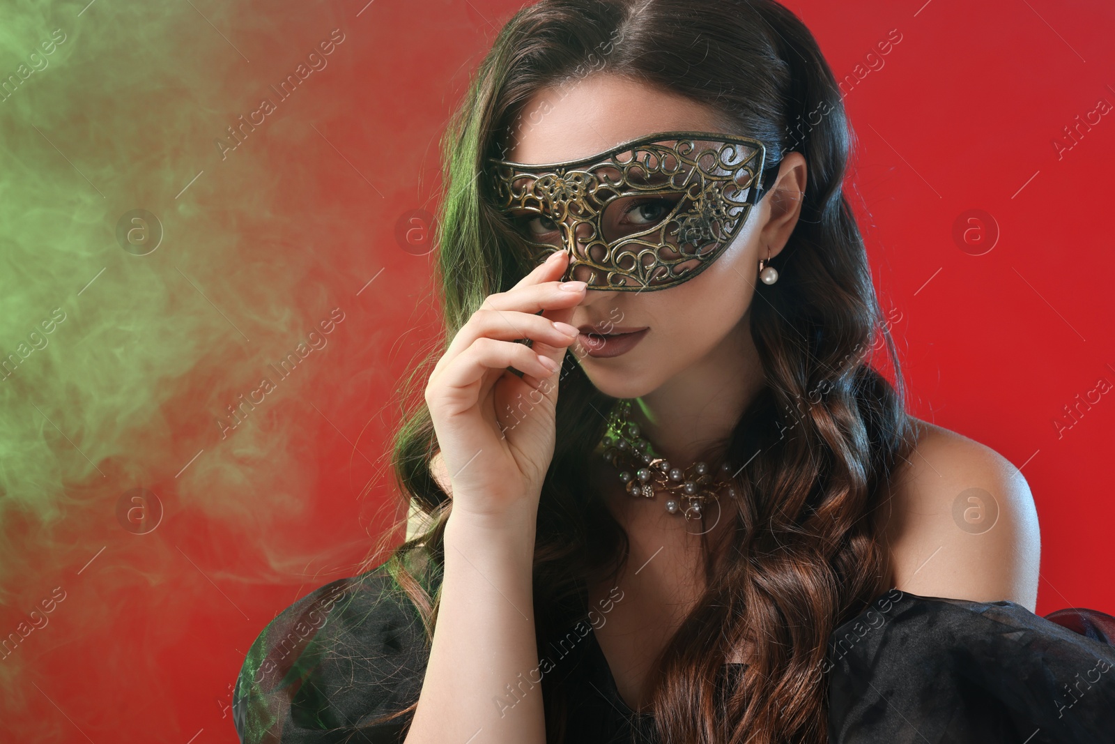 Photo of Beautiful woman wearing carnival mask on red background in color lights and smoke