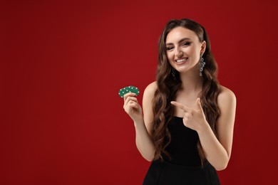 Photo of Smiling woman pointing at poker chips on red background. Space for text