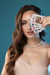 Photo of Poker game. Charming woman covering eye with playing cards on light blue background