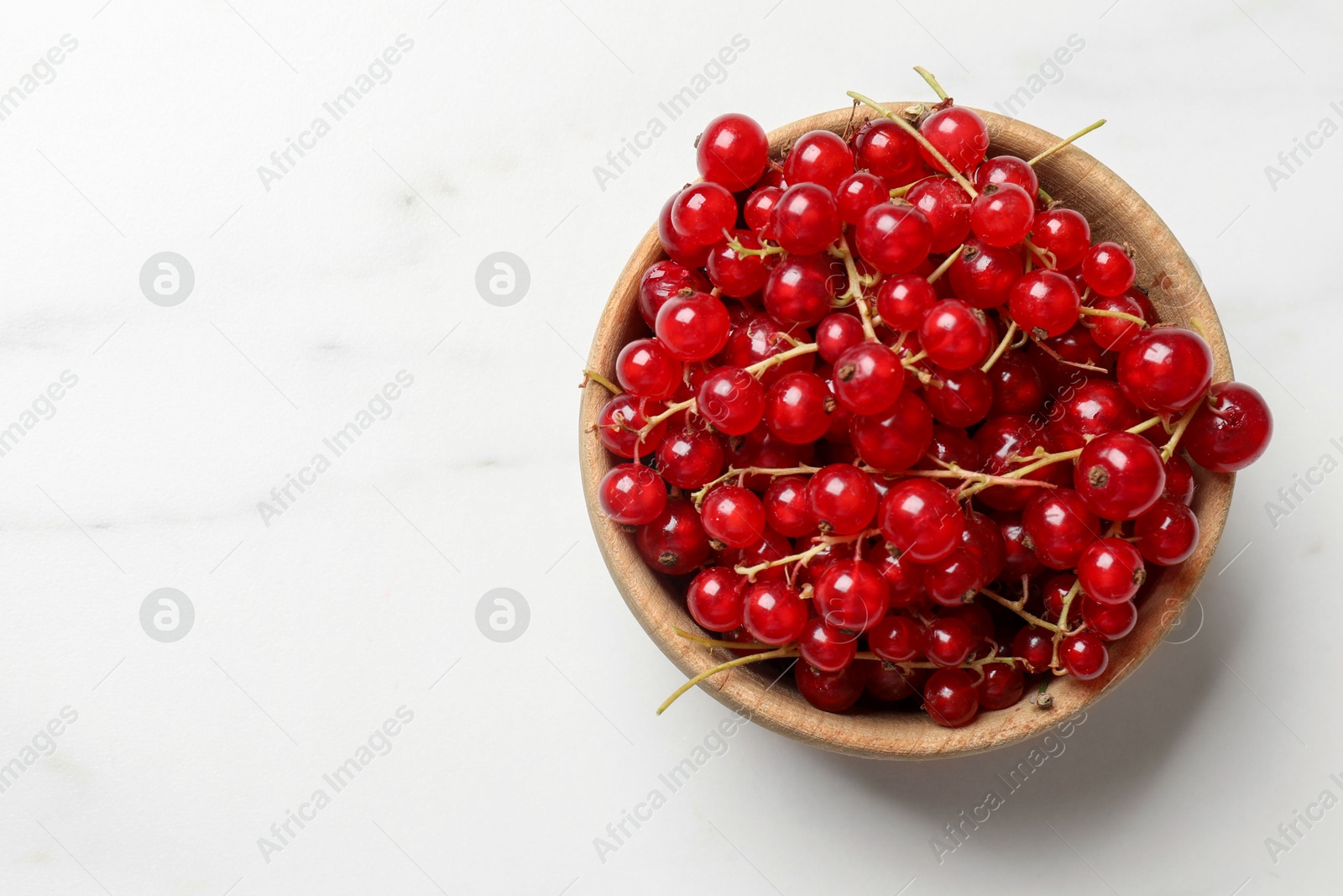 Photo of Fresh red currant berries in bowl on white table, top view. Space for text