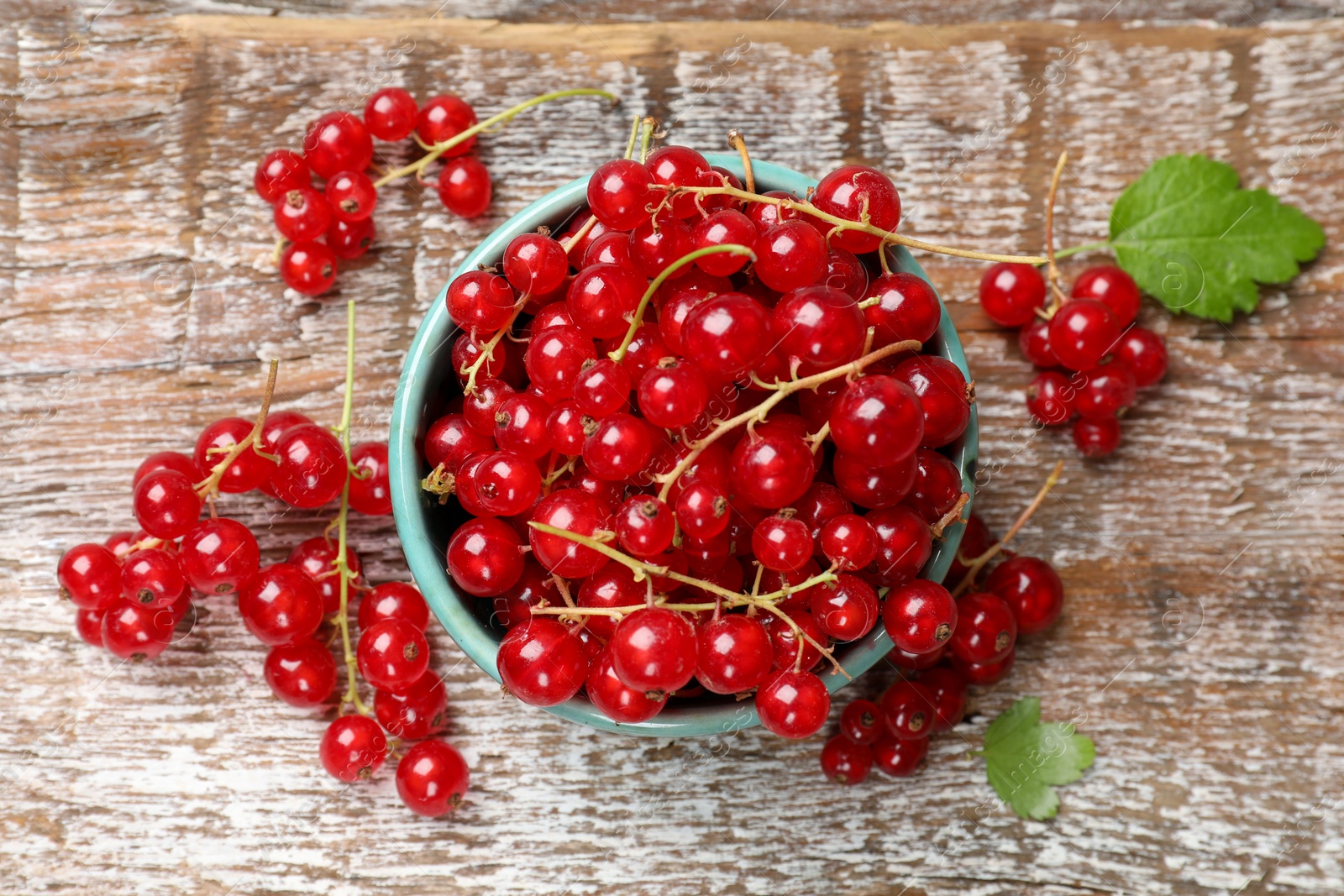 Photo of Fresh red currant berries in bowl on wooden table, top view