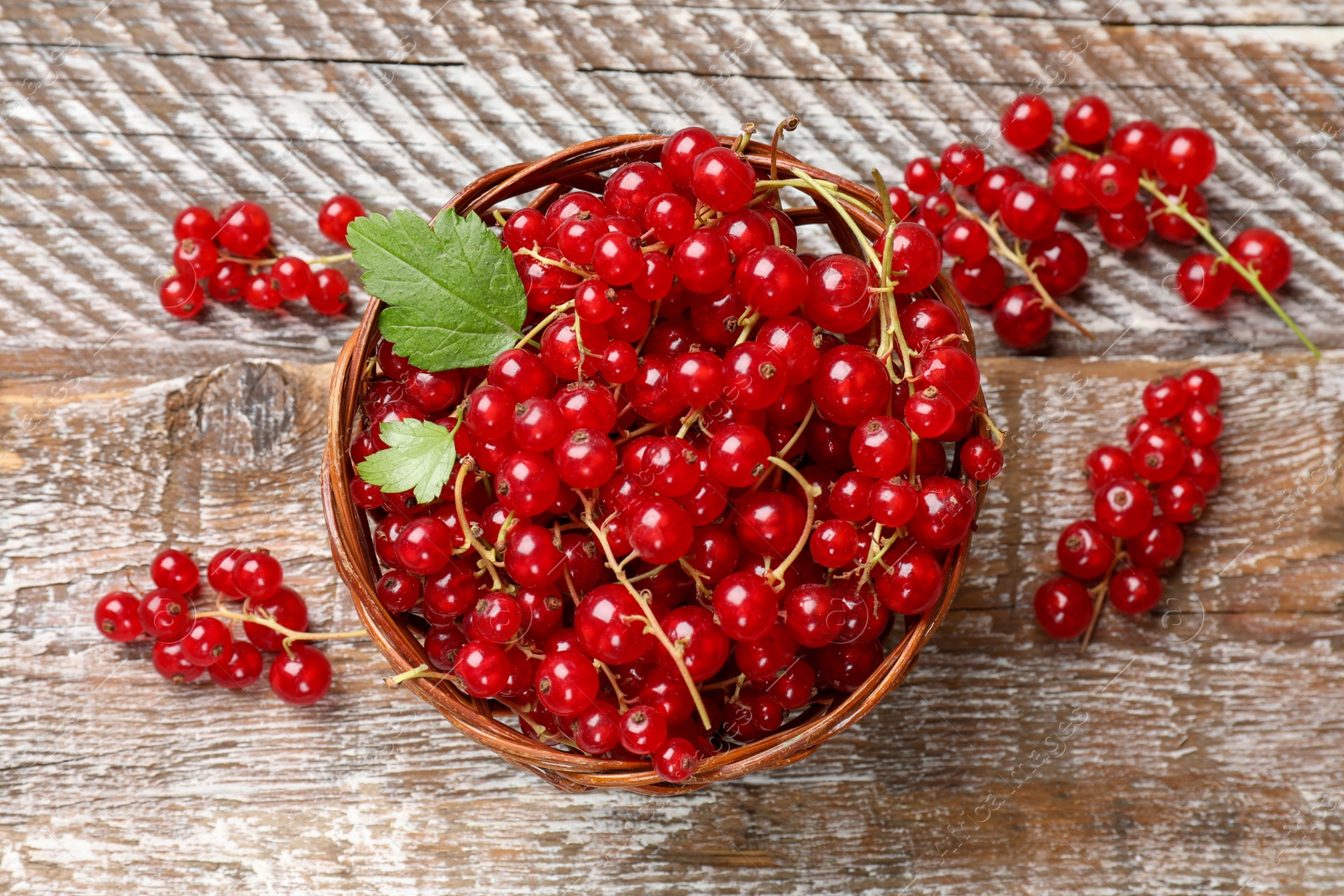 Photo of Fresh red currant berries in basket on wooden table, top view