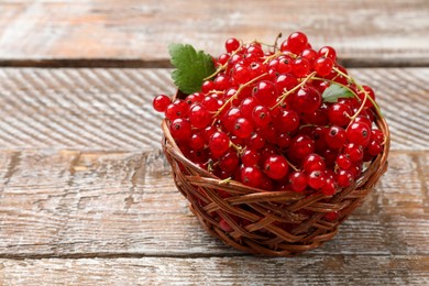 Photo of Fresh red currant berries in basket on wooden table, closeup