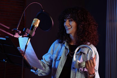 Photo of Singer with headphones and sheets recording song in professional record studio