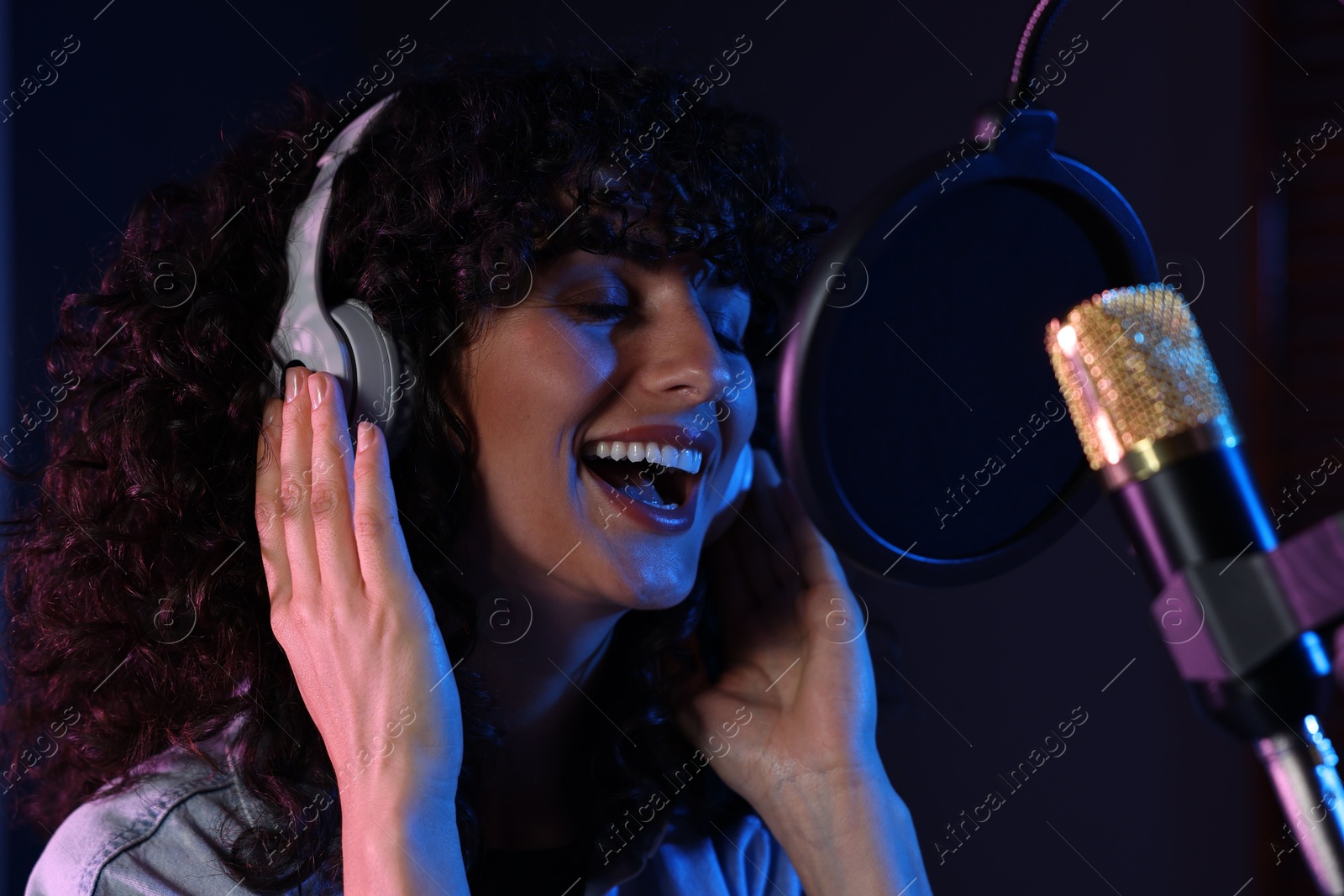 Photo of Vocalist with headphones singing into microphone in professional record studio