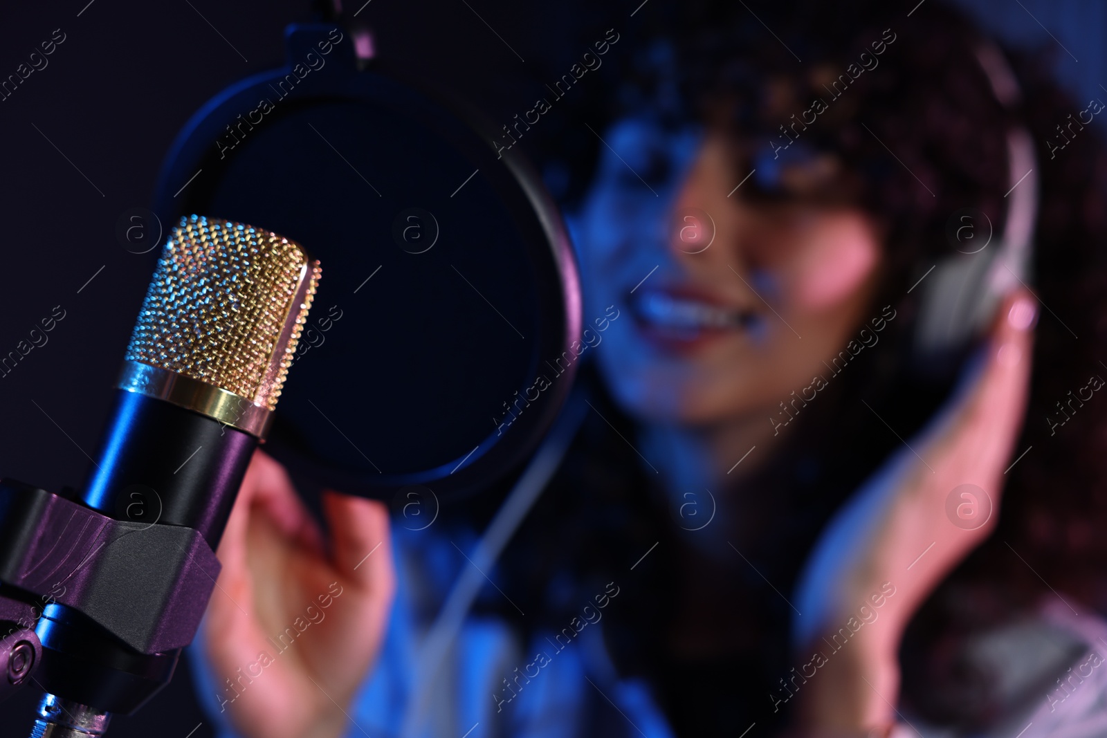 Photo of Woman singing into microphone in professional record studio, selective focus