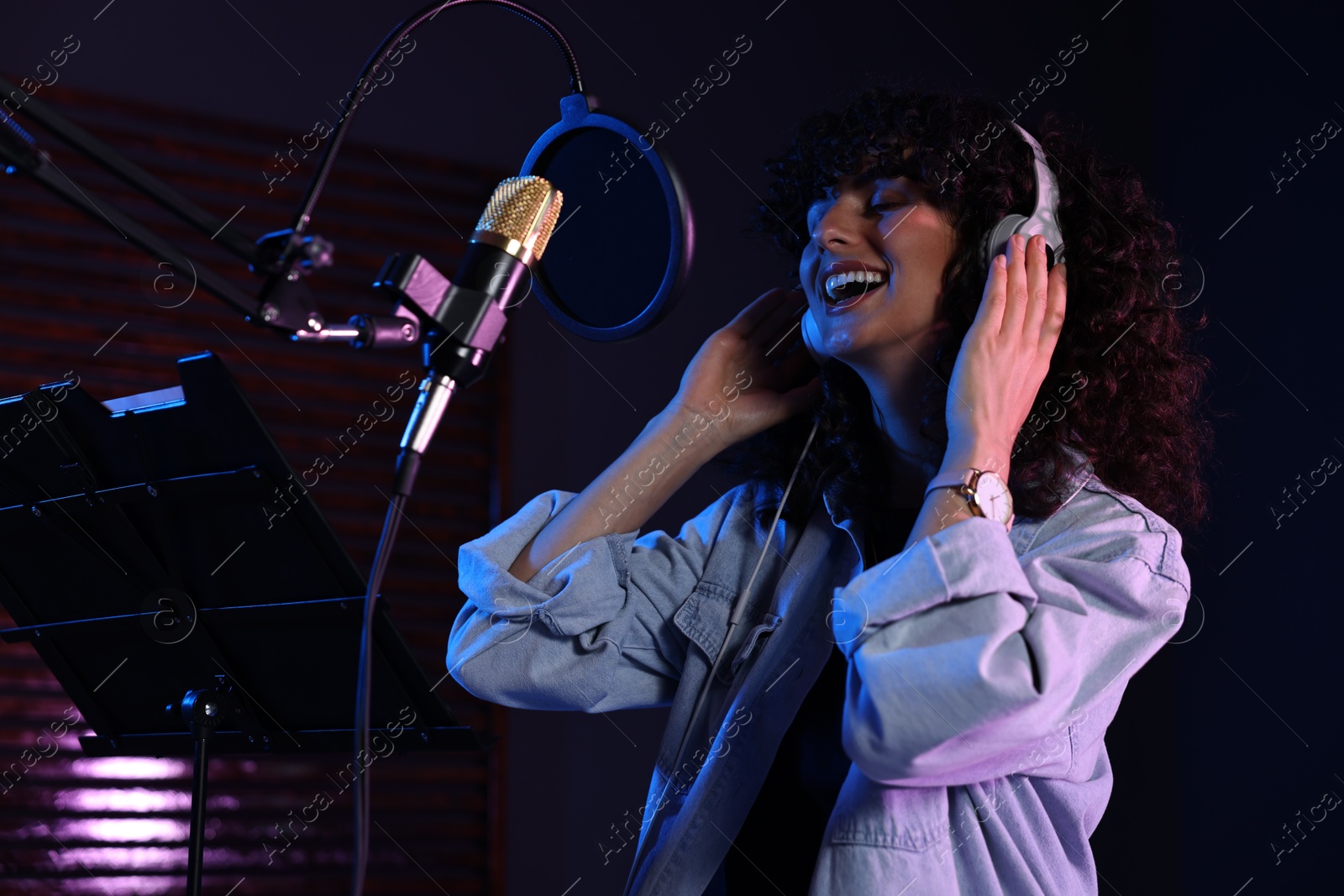 Photo of Vocalist with headphones singing into microphone in professional record studio