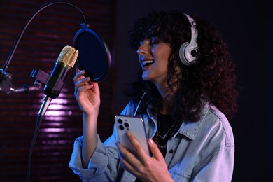 Photo of Vocalist with smartphone singing into microphone in professional record studio