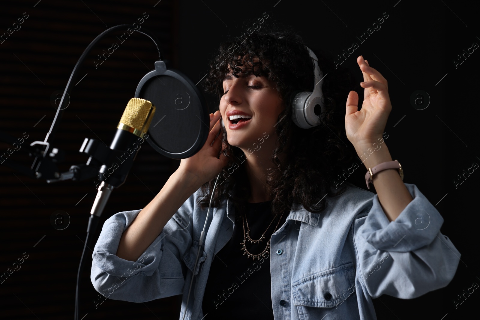 Photo of Vocalist with headphones singing into microphone in professional record studio