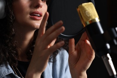Photo of Woman singing into microphone in professional record studio, closeup
